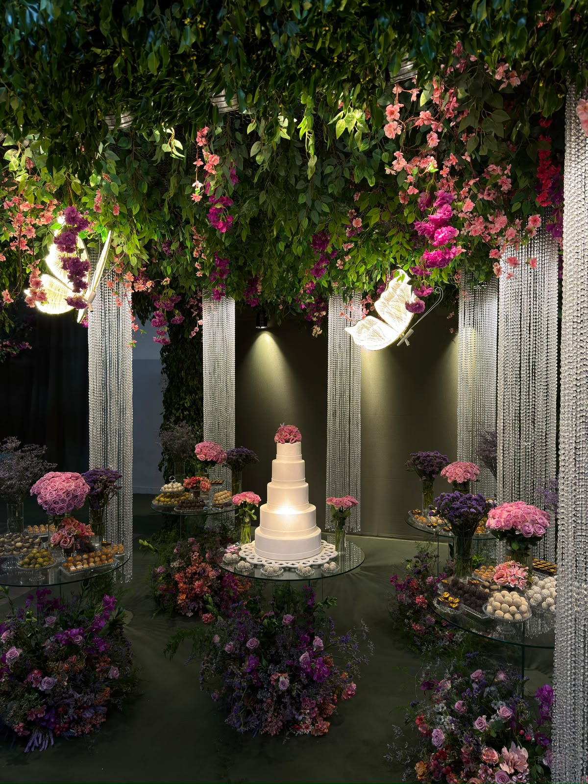 Mesa de casamento em jardim iluminado com bolo alto e borboletas